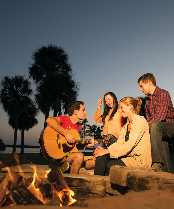 Eckerd students around a bonfire on beach with guitar in 2015