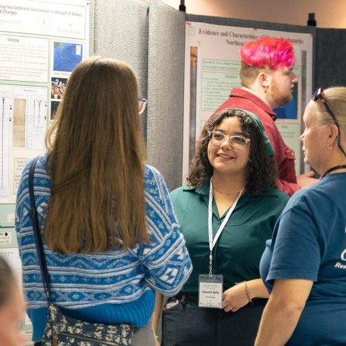 Student wearing badge explains materials on her poster to visitors
