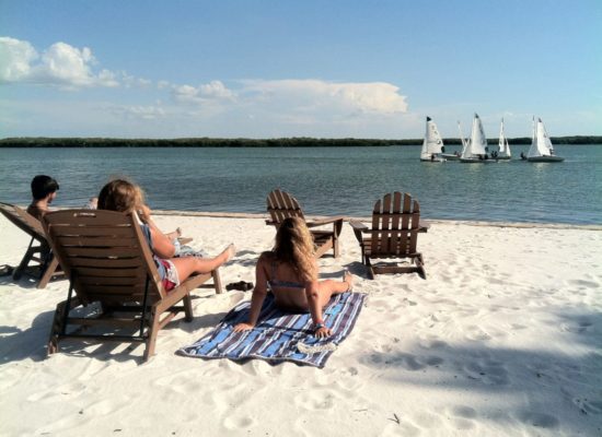 Three students laying on the beach studying while sailboats go by